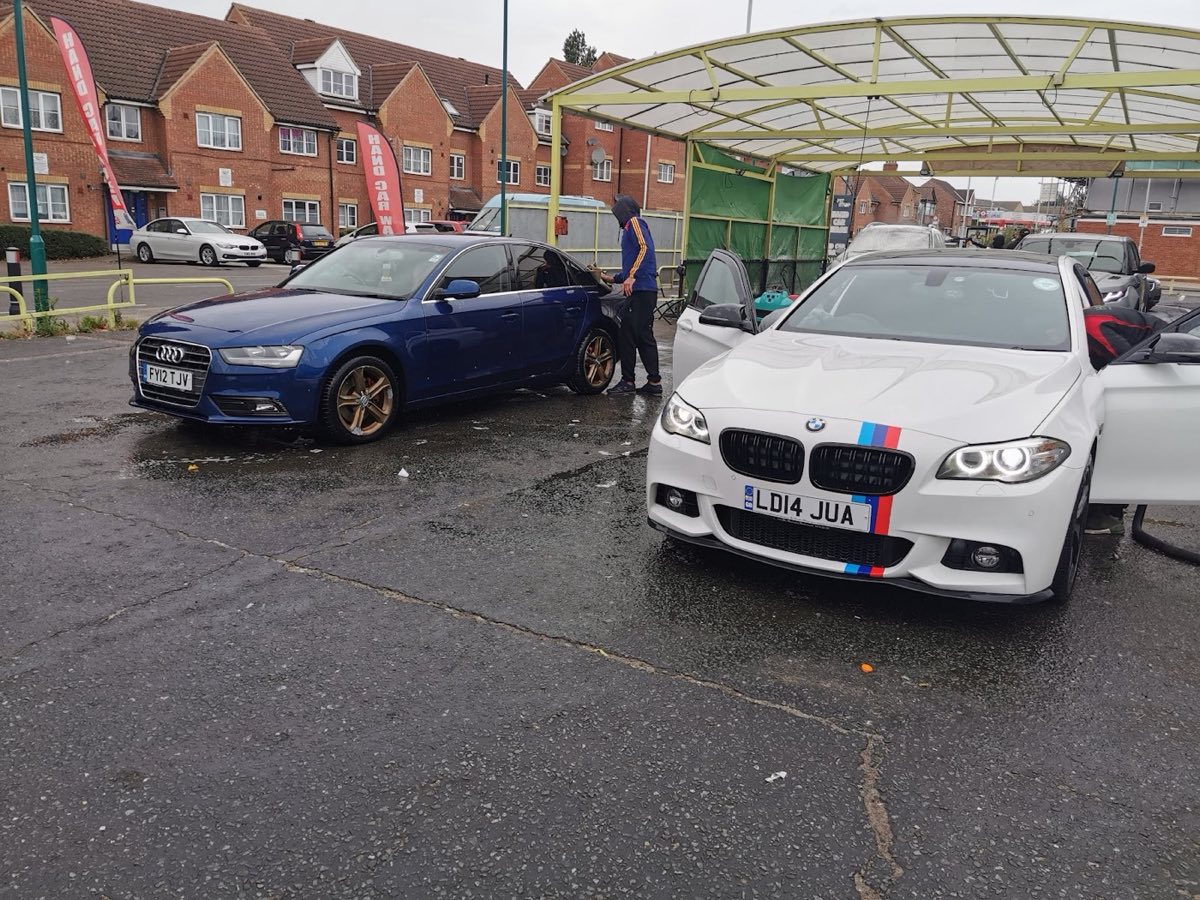 A blue Audi saloon and a white BMW with an M-stripe being cleaned side by side on the Pit Stop pitch in Newbury Park.