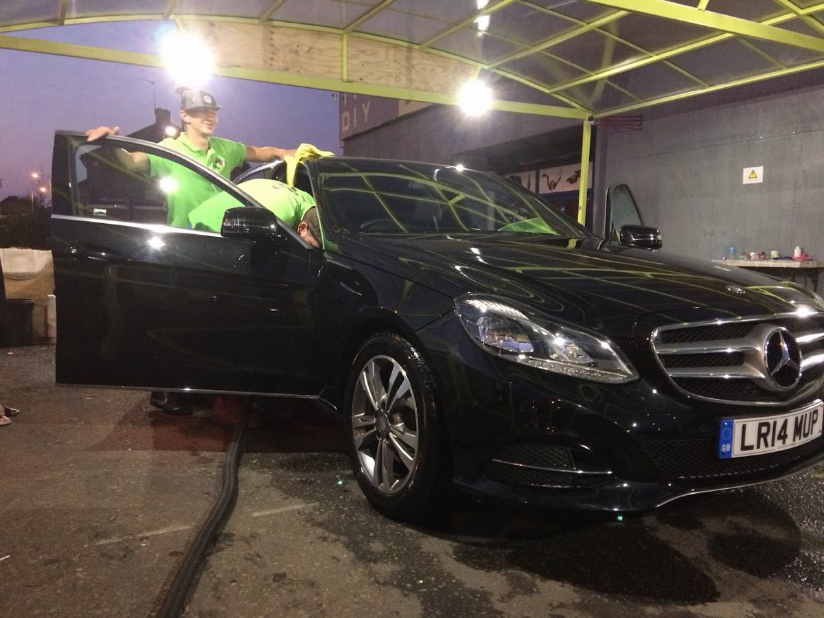A black Mercedes E-Class being hand-dried under the lit canopy at Pit Stop in the evening, paintwork reflecting the lights.